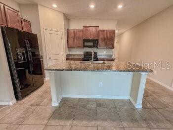 A kitchen features dark wood cabinets, granite countertops, a central island, and a black refrigerator — 17132 WHITE MANGROVE DRIVE, WIMAUMA, FL