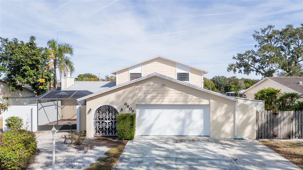 A two-story house with light-colored siding, a white garage door, and a decorative metal gate — 6809 TWELVE OAKS BOULEVARD, TAMPA, FL