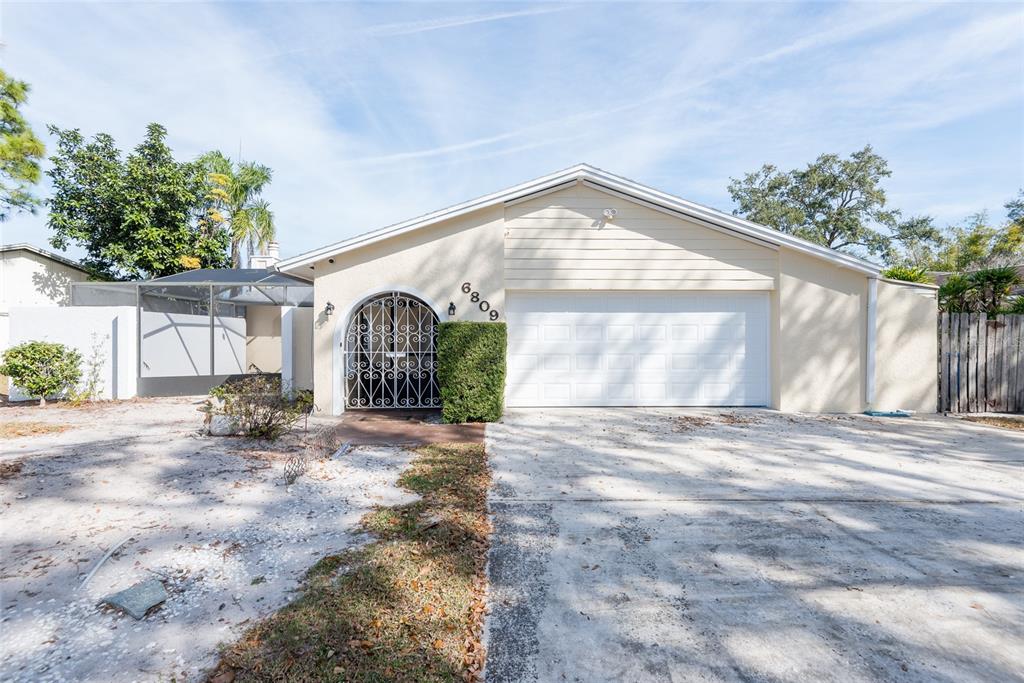 A single-story house with a beige exterior, a white garage door, and a gated entryway — 6809 TWELVE OAKS BOULEVARD, TAMPA, FL