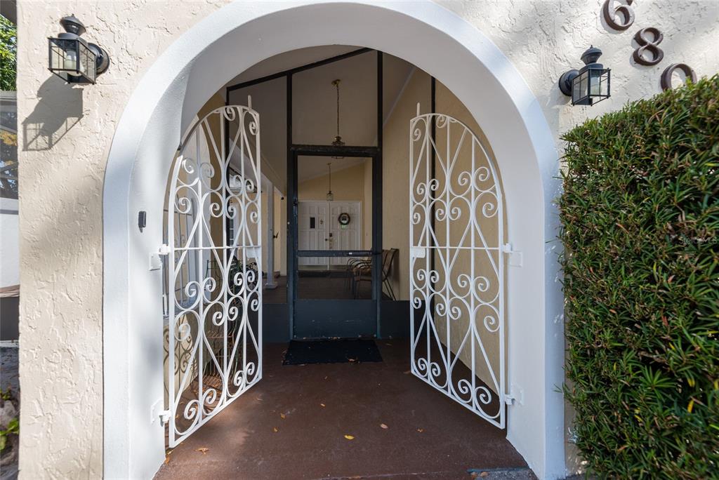 An arched entryway features white decorative metal gates opening to a screened porch — 6809 TWELVE OAKS BOULEVARD, TAMPA, FL