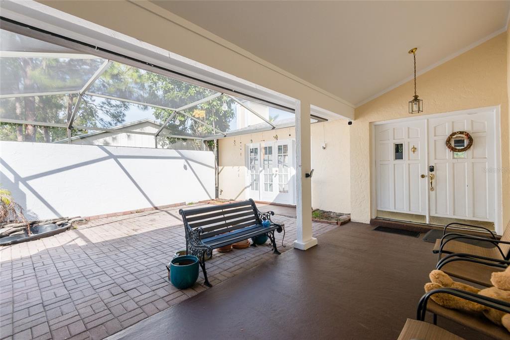 A covered patio features a brick floor, a black bench, and double white entry doors — 6809 TWELVE OAKS BOULEVARD, TAMPA, FL