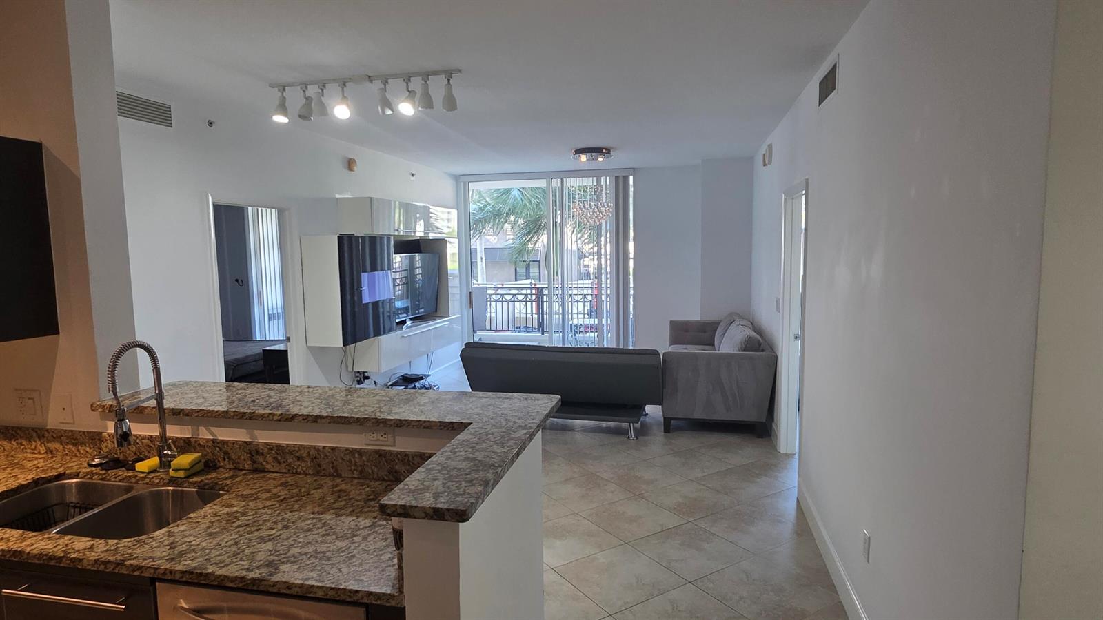 A kitchen with granite countertops overlooks a living room featuring a sofa and balcony access — 550 Okeechobee Boulevard # 308, West Palm Beach FL 33401, WEST PALM BEACH, FL