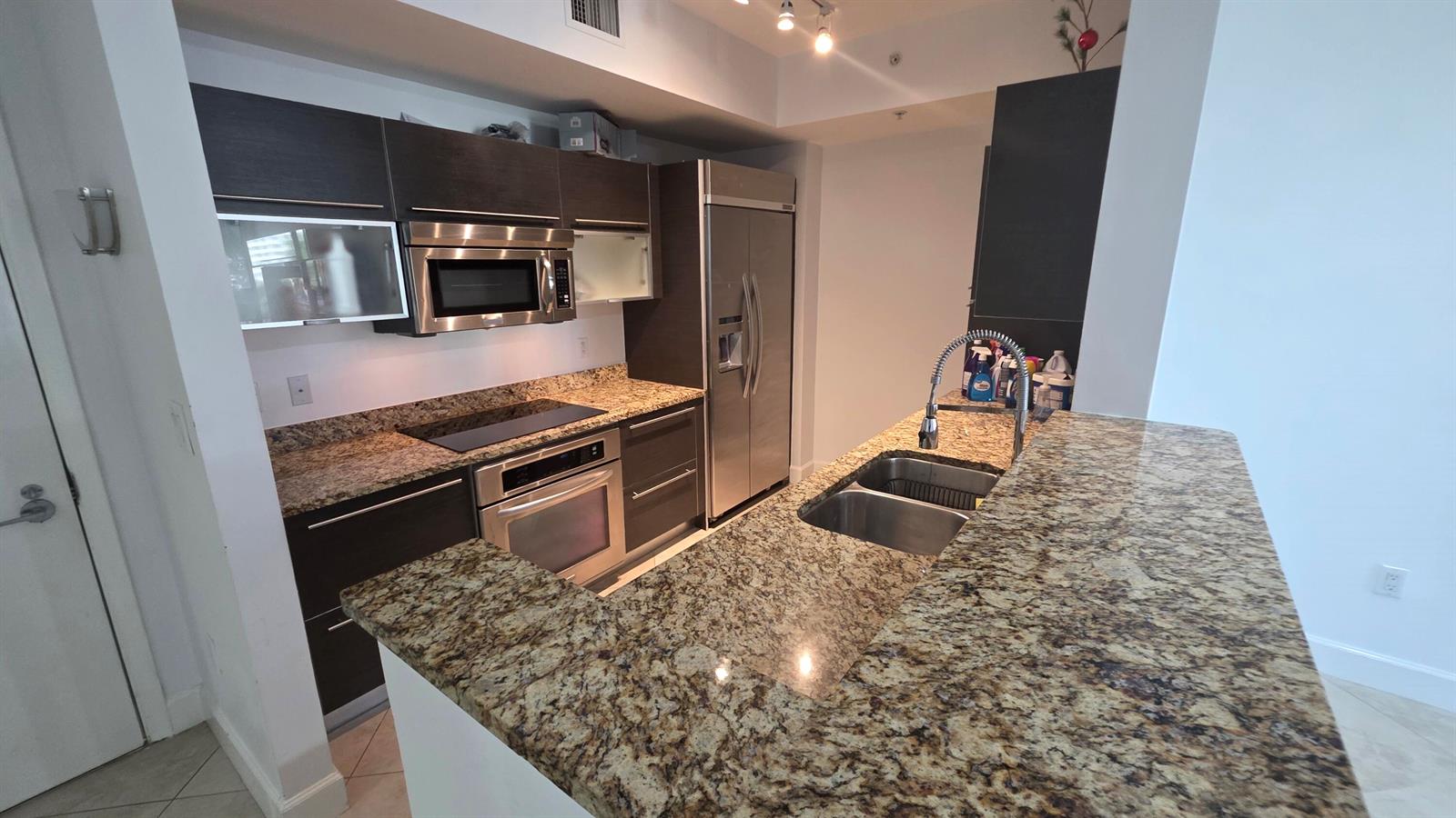 A kitchen features dark wood cabinets, granite countertops, stainless steel appliances, and a double sink — 550 Okeechobee Boulevard # 308, West Palm Beach FL 33401, WEST PALM BEACH, FL