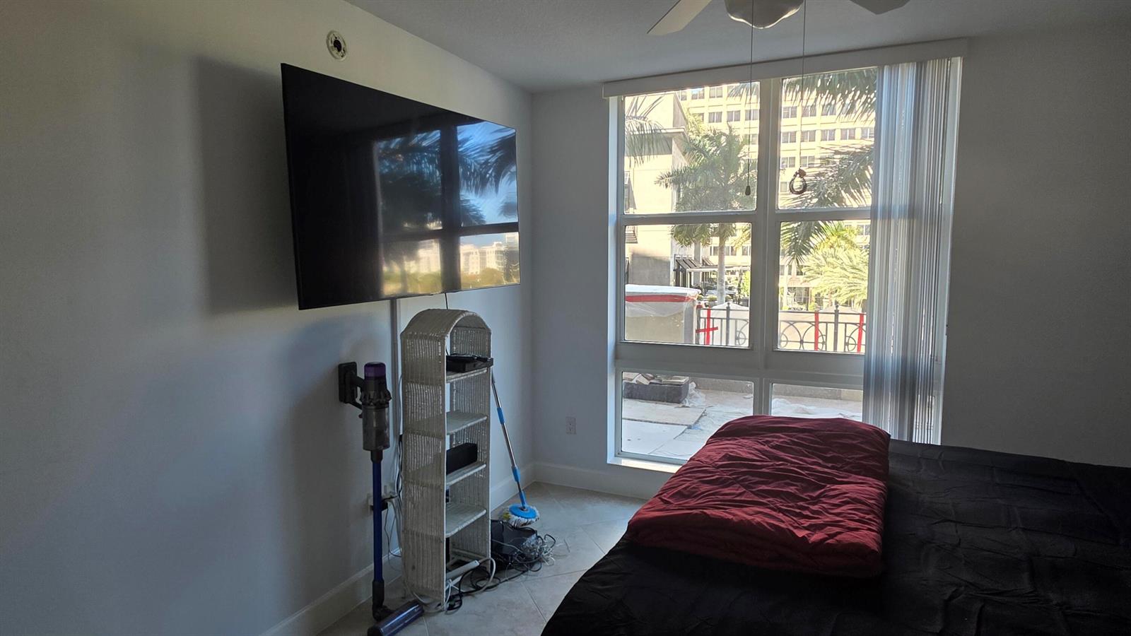 A bedroom features a wall-mounted television, a white wicker shelf, and a large window view — 550 Okeechobee Boulevard # 308, West Palm Beach FL 33401, WEST PALM BEACH, FL