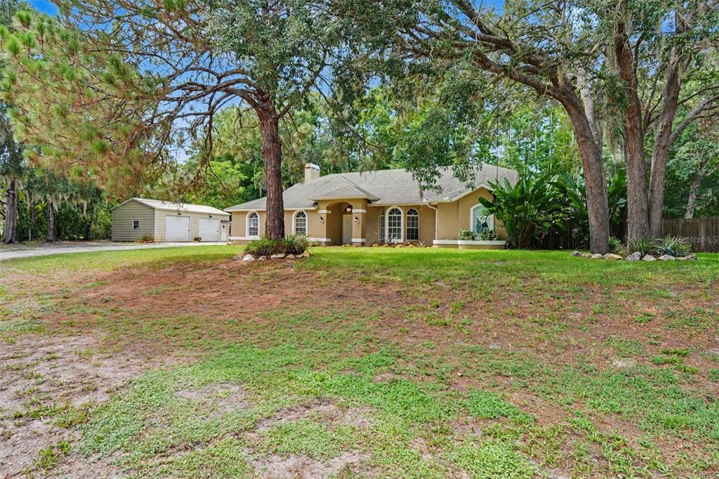 A single-story tan house with a detached garage sits on a grassy, tree-filled lot — 10551 CASEY DRIVE, NEW PORT RICHEY, FL
