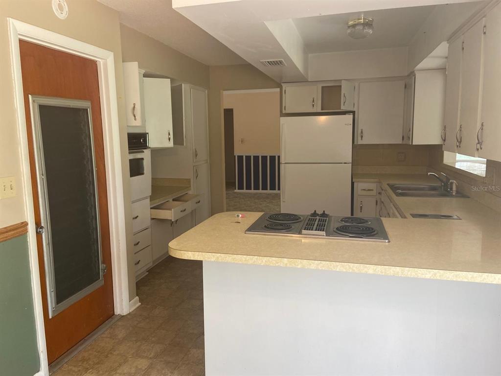 A kitchen features white cabinets, a white refrigerator, a drop-in cooktop, and laminate countertops — 4059 S LINWOOD TERRACE, INVERNESS, FL