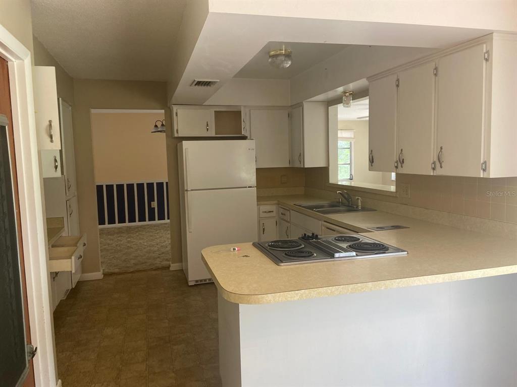 A kitchen features white cabinets, laminate countertops, a drop-in cooktop, and a white refrigerator — 4059 S LINWOOD TERRACE, INVERNESS, FL
