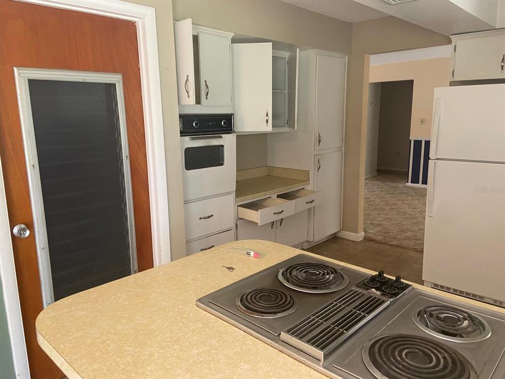 A kitchen features white cabinets, a built-in oven, a cooktop island, and a refrigerator — 4059 S LINWOOD TERRACE, INVERNESS, FL