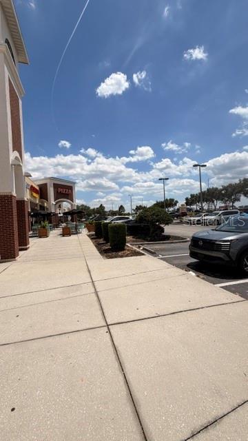 A sidewalk leads past a brick building toward a shopping center parking lot under blue skies — 42601 HIGHWAY 27, DAVENPORT, FL
