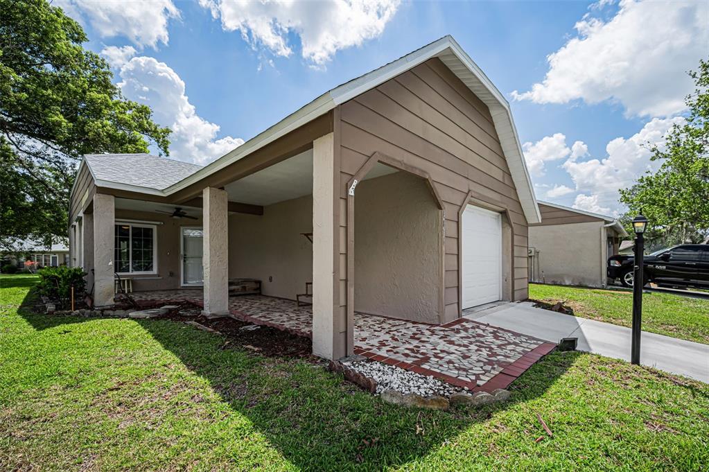 A tan house exterior features a covered patio, a single-car garage, and a paved walkway — 4876 BOONESBORO COURT, NEW PORT RICHEY, FL