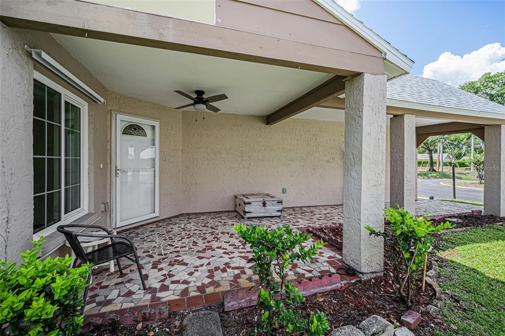 A covered patio features a mosaic tile floor, a ceiling fan, and a white door — 4876 BOONESBORO COURT, NEW PORT RICHEY, FL