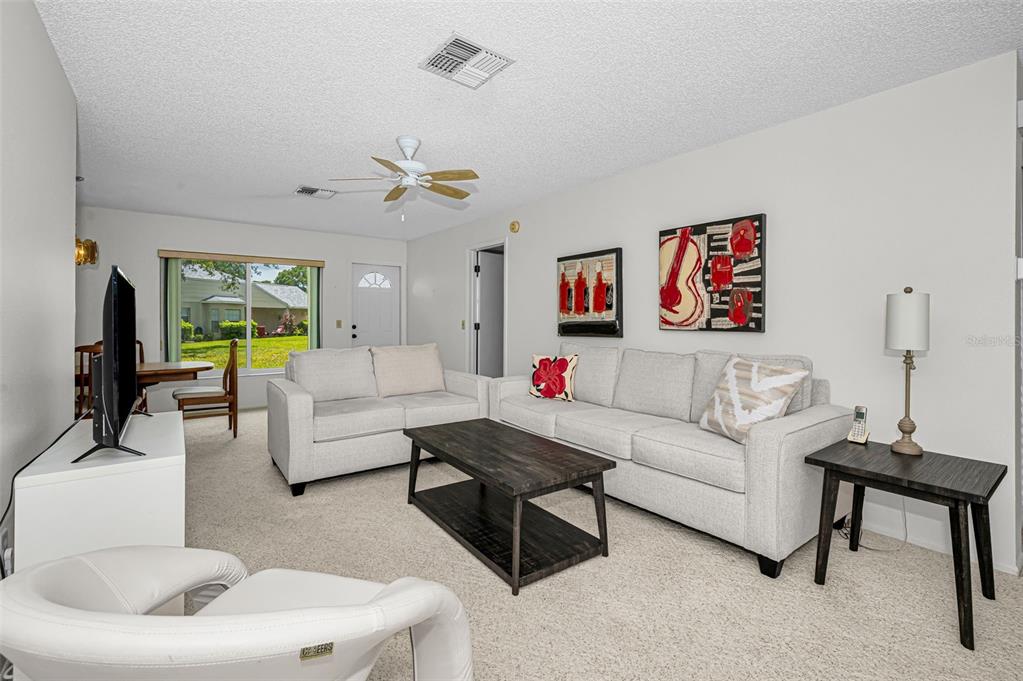 A living room features light-colored sofas, a dark wood coffee table, and abstract wall art — 4876 BOONESBORO COURT, NEW PORT RICHEY, FL