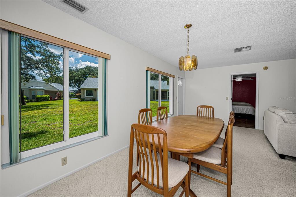 A dining room with a wooden table, chairs, carpeted floors, and two large windows — 4876 BOONESBORO COURT, NEW PORT RICHEY, FL