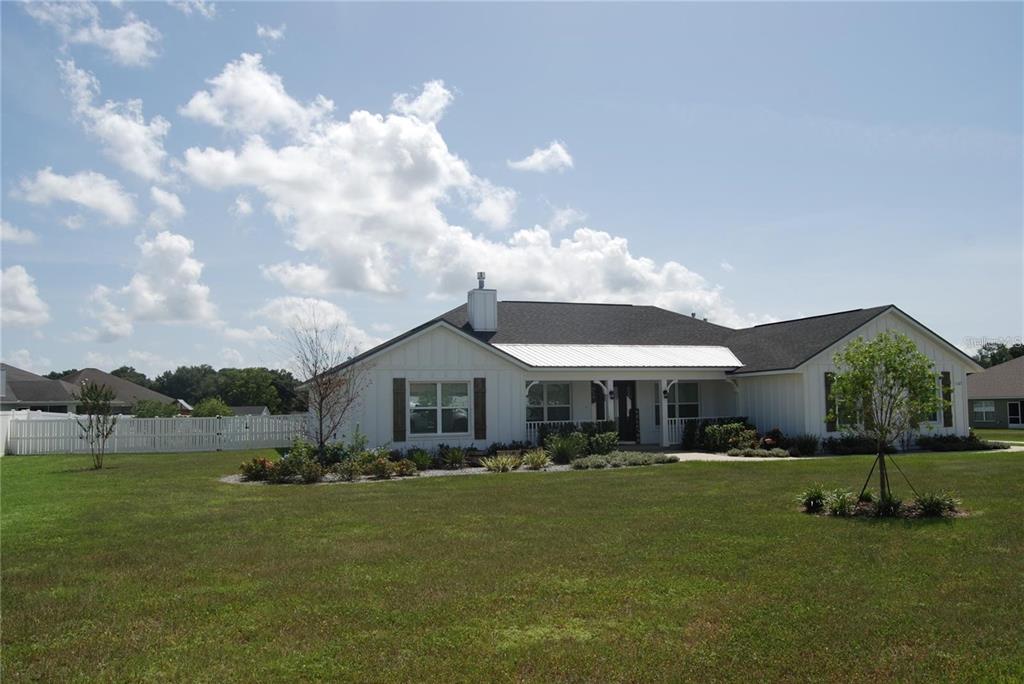 A white farmhouse-style house with a dark roof sits on a large, grassy lawn — 1167 SE 63RD COURT ROAD, OCALA, FL