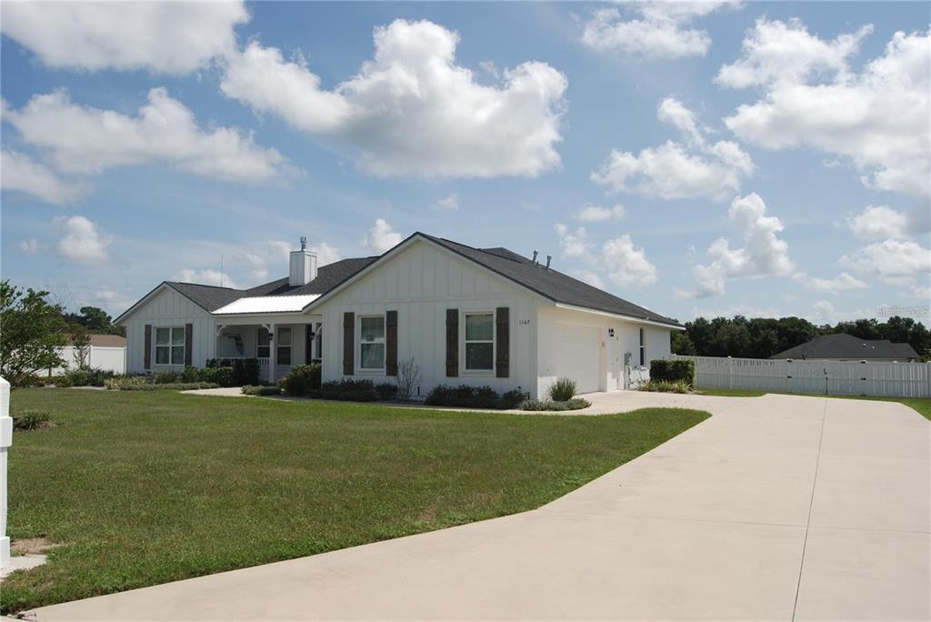 A white single-story house with a dark roof and a concrete driveway under a cloudy sky — 1167 SE 63RD COURT ROAD, OCALA, FL