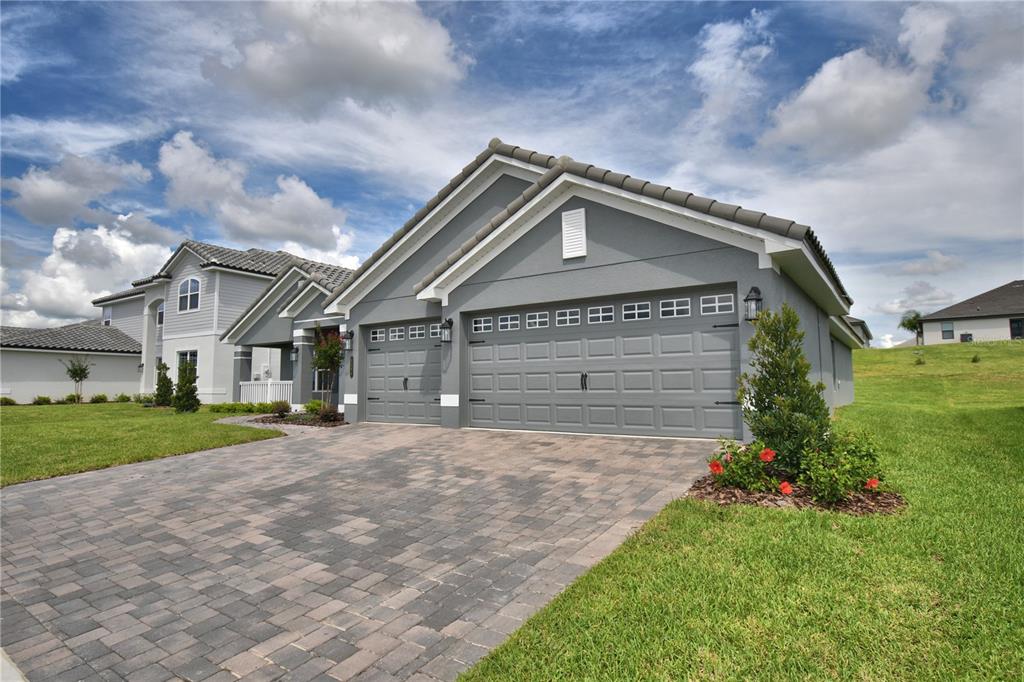 A gray house with a three-car garage and a paved driveway under a cloudy sky — 5421 WATERSIDE DRIVE, AUBURNDALE, FL