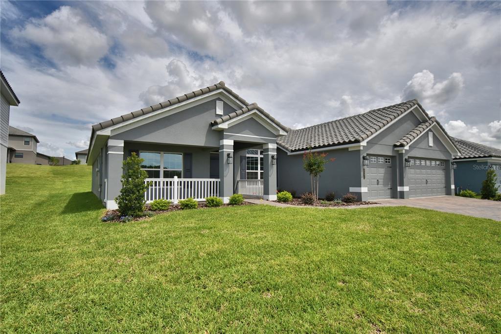 A gray single-story house with a white porch railing, tiled roof, and a two-car garage — 5421 WATERSIDE DRIVE, AUBURNDALE, FL
