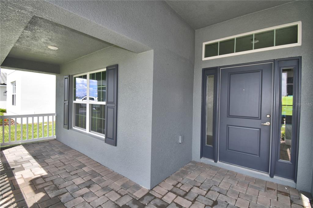 A covered porch with paver flooring leads to a dark blue front door with sidelights — 5421 WATERSIDE DRIVE, AUBURNDALE, FL