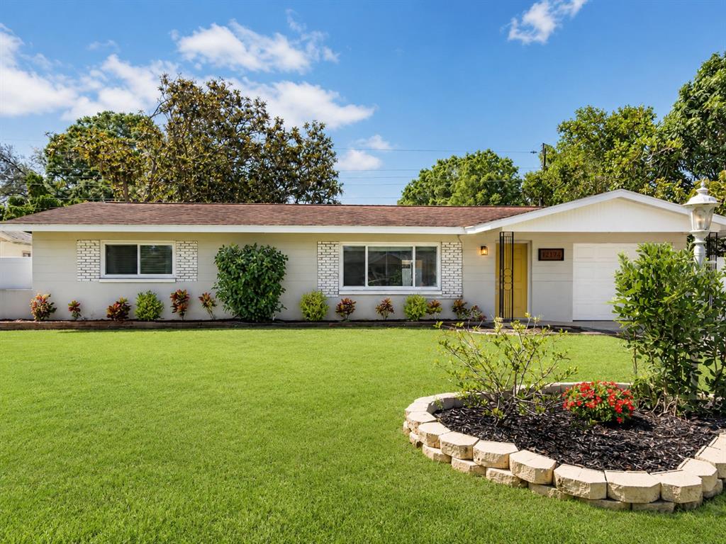 A single-story house with a light-colored exterior, a yellow front door, and a front lawn — 12174 83RD AVENUE, SEMINOLE, FL