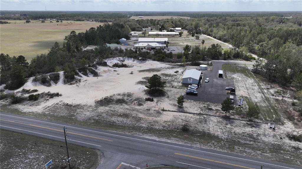 An aerial view shows a commercial building with a parking lot and a sandy lot — 106 SHRINE CLUB ROAD, POMONA PARK, FL
