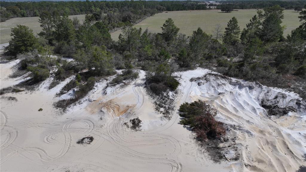 An aerial view shows a sandy, unpaved area with tire tracks bordered by trees and fields — 106 SHRINE CLUB ROAD, POMONA PARK, FL