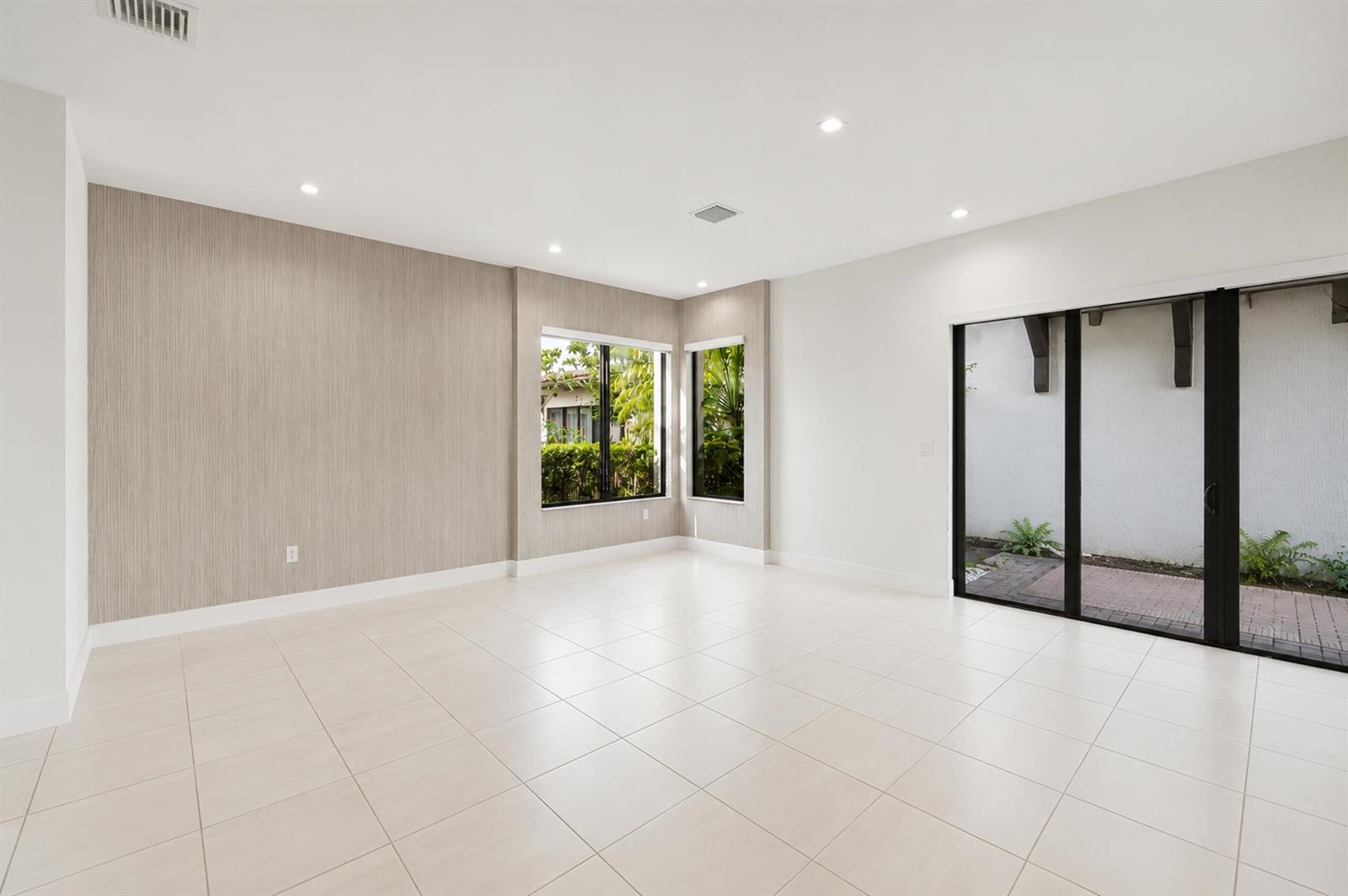 A bright, empty room features light-colored tile flooring, textured accent walls, and sliding glass doors — 8272 NW 44th Terrace, Doral FL 33166, DORAL, FL