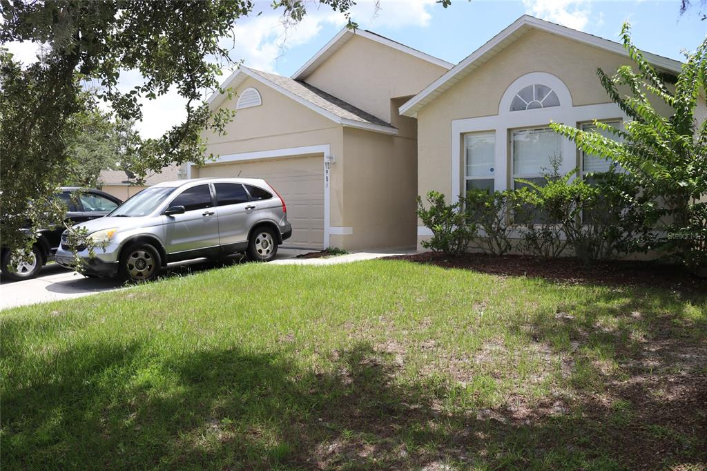 A beige single-story house with a two-car garage and a silver SUV in the driveway — 1983 PERIDOT CIRCLE, KISSIMMEE, FL