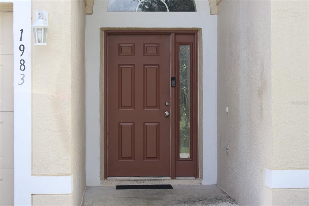 A brown front door with a side window and house number 1983 on the wall — 1983 PERIDOT CIRCLE, KISSIMMEE, FL