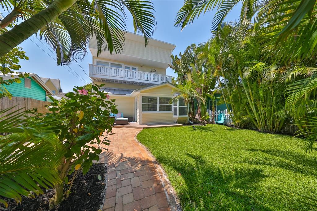 A backyard with a brick walkway, a grassy lawn, palm trees, and a yellow house — 13004 BOCA CIEGA AVENUE, MADEIRA BEACH, FL