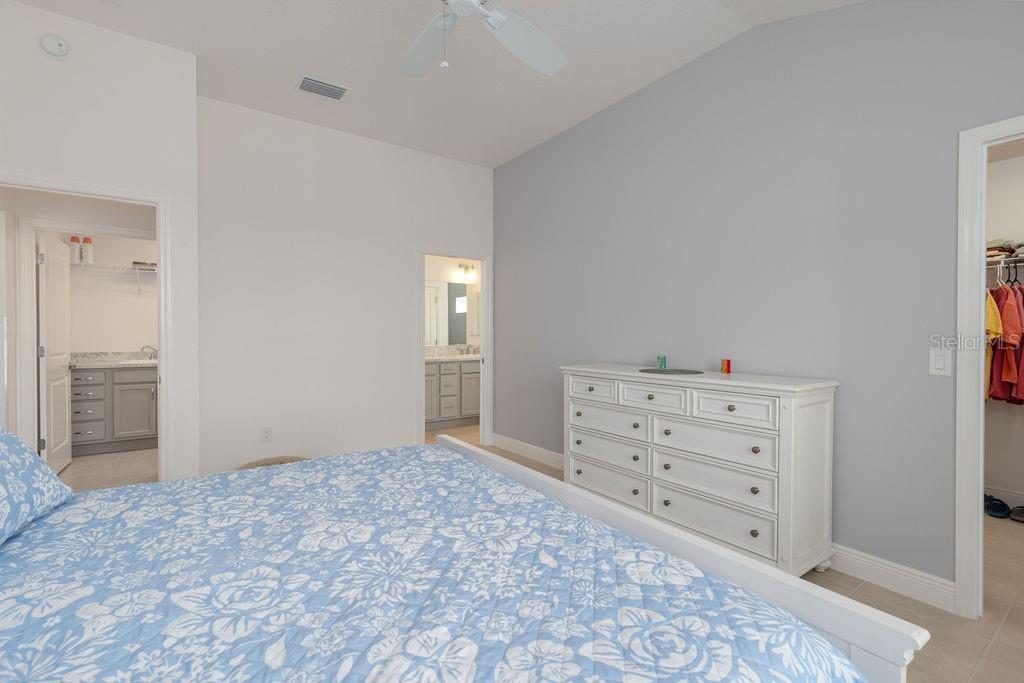 A bedroom features a blue floral bedspread, a white dresser, and two doorways leading elsewhere — 2454 YOUNGMANN LOOP, THE VILLAGES, FL