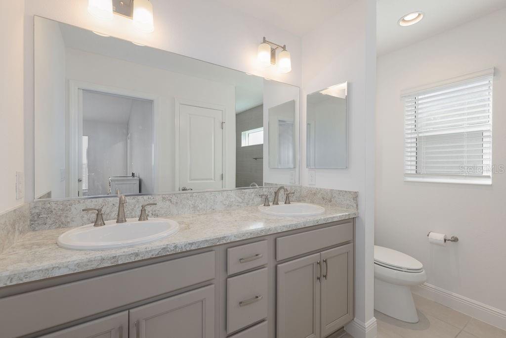 A bathroom features a double vanity with a stone countertop, gray cabinets, and a large mirror — 2454 YOUNGMANN LOOP, THE VILLAGES, FL
