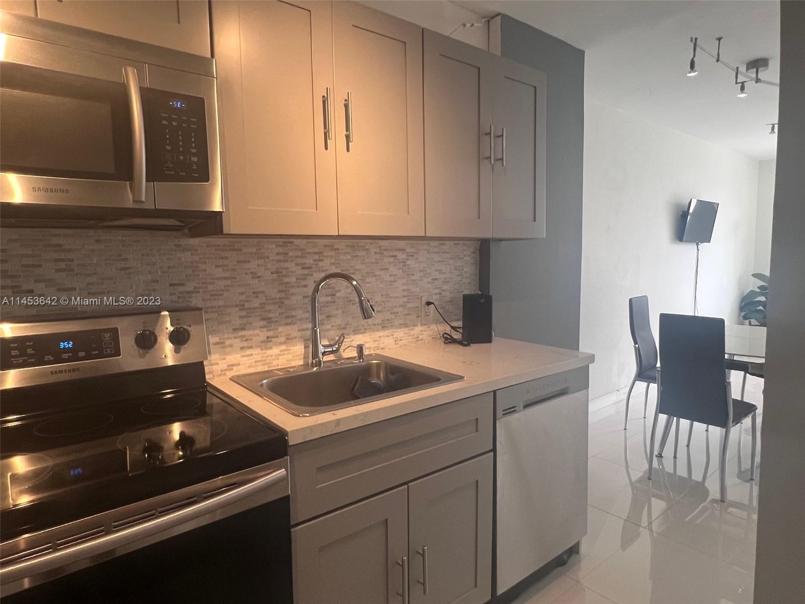 A kitchen features gray cabinets, stainless steel appliances, a tiled backsplash, and a white countertop — 100 Lincoln Rd # 501, Miami Beach FL 33139, MIAMI BEACH, FL