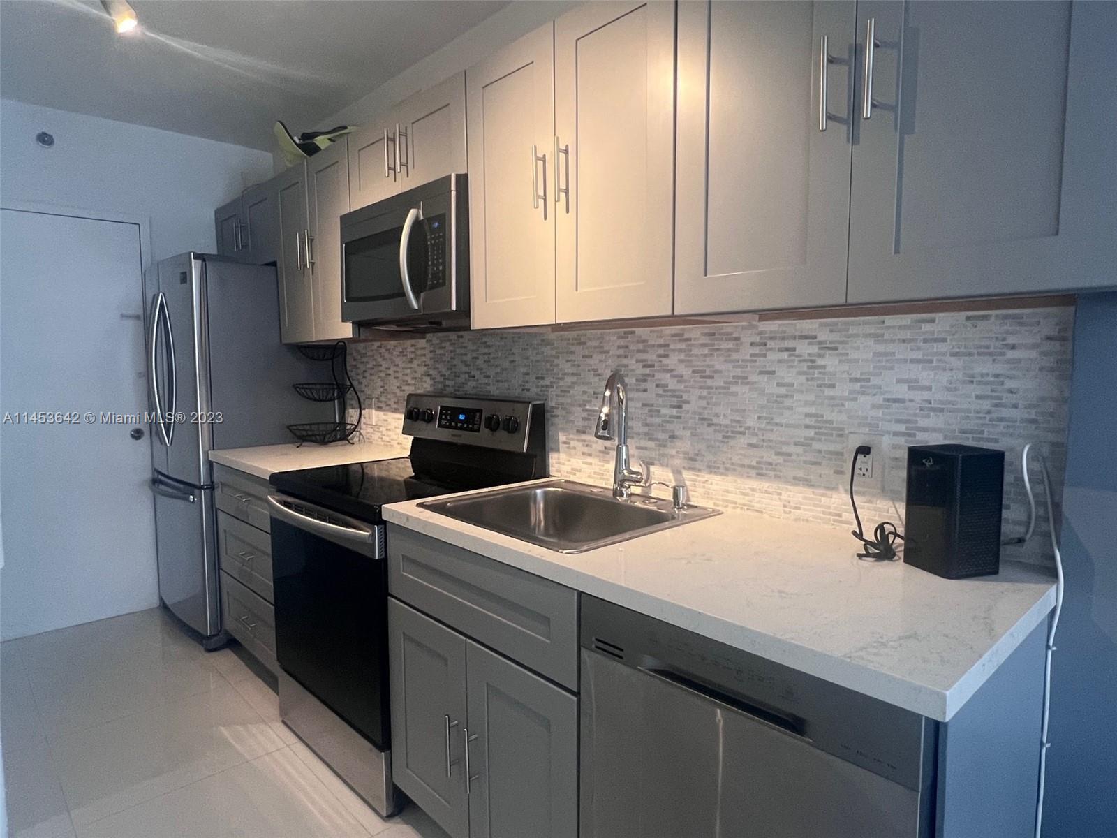 A kitchen features gray cabinets, stainless steel appliances, white countertops, and a tiled backsplash — 100 Lincoln Rd # 501, Miami Beach FL 33139, MIAMI BEACH, FL