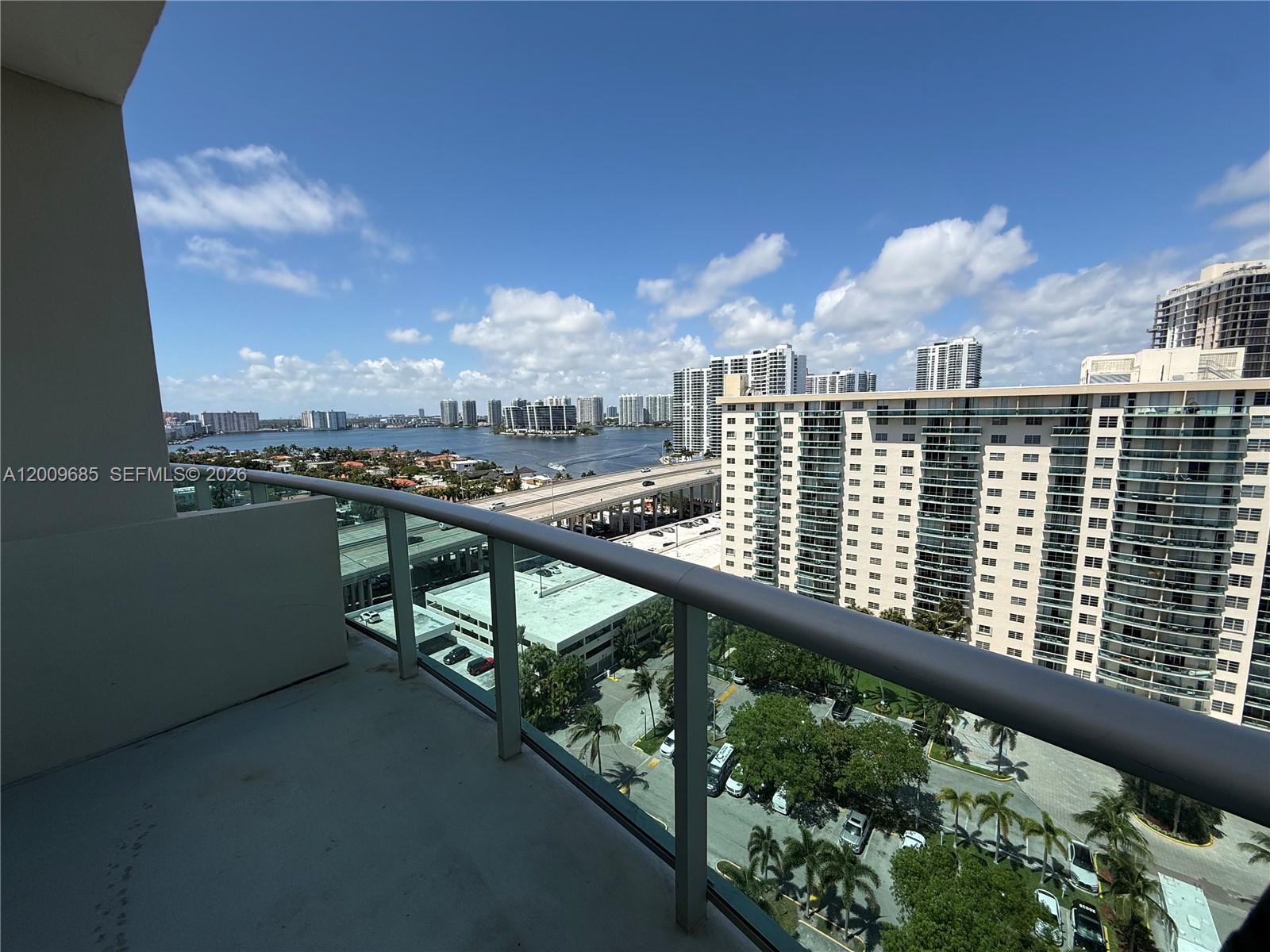 A high-rise balcony overlooks a parking lot, a highway, a waterway, and city buildings — SUNNY ISLES BEACH, FL