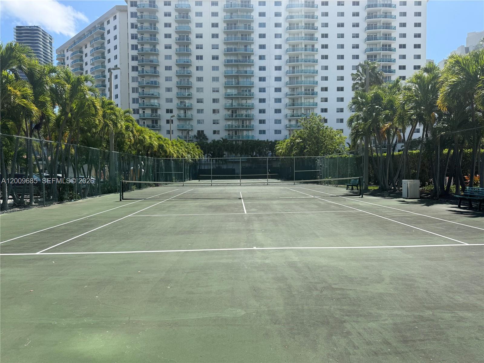 A tennis court sits in front of a tall residential building surrounded by palm trees — SUNNY ISLES BEACH, FL