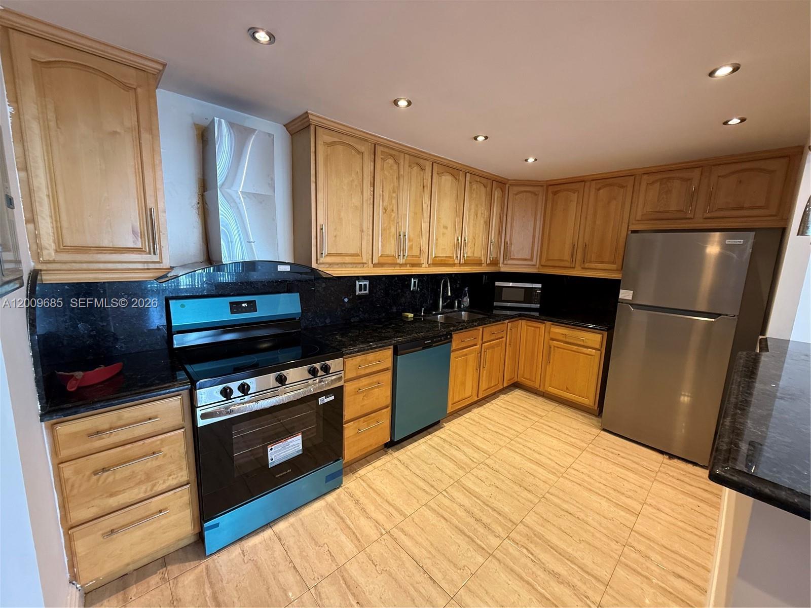A kitchen features light wood cabinets, black granite countertops, stainless steel appliances, and tiled flooring — SUNNY ISLES BEACH, FL