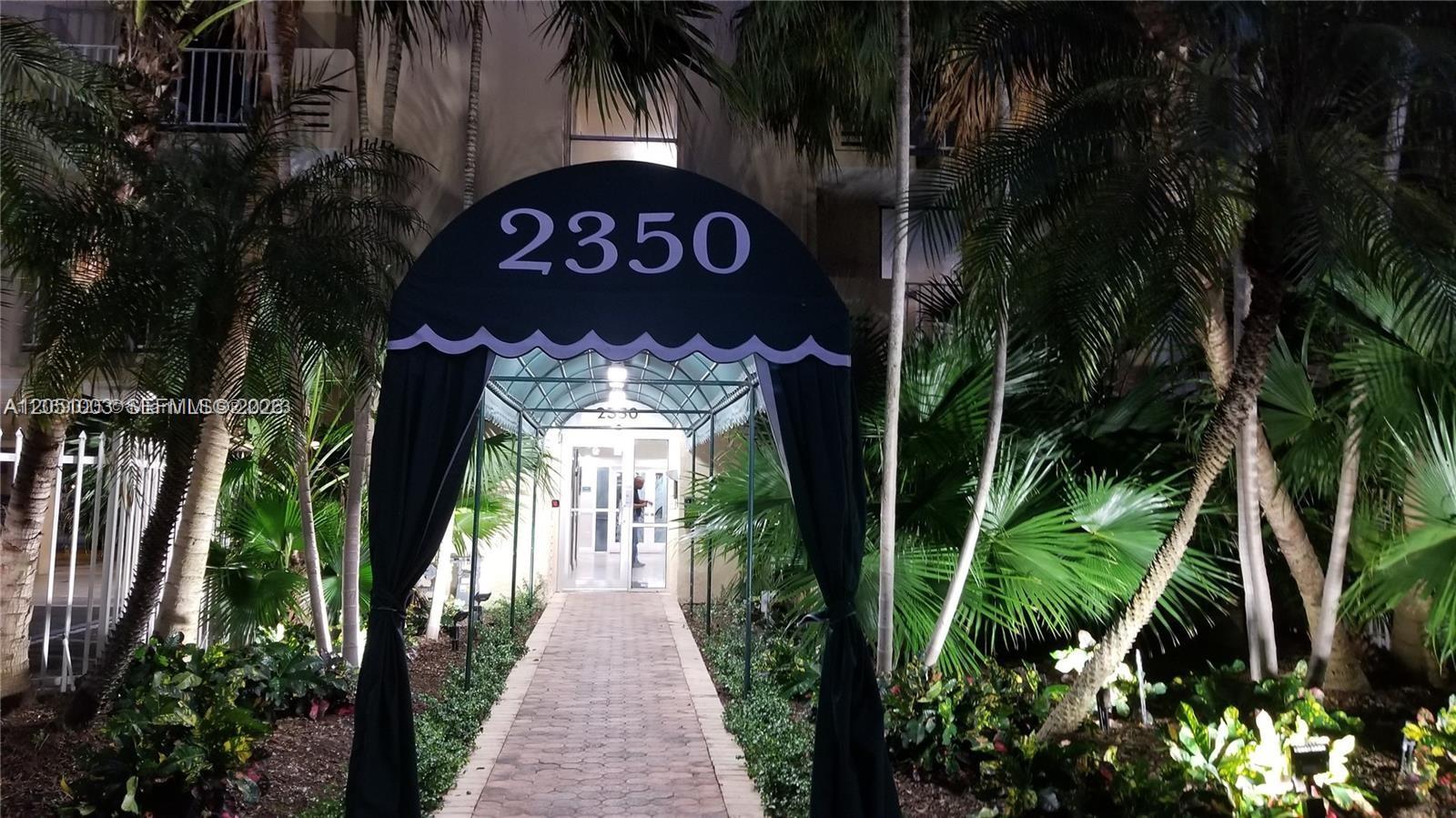 A paved walkway leads to a building entrance covered by a black arched canopy — 2350 NE 135th St # 403, North Miami FL 33181, NORTH MIAMI, FL