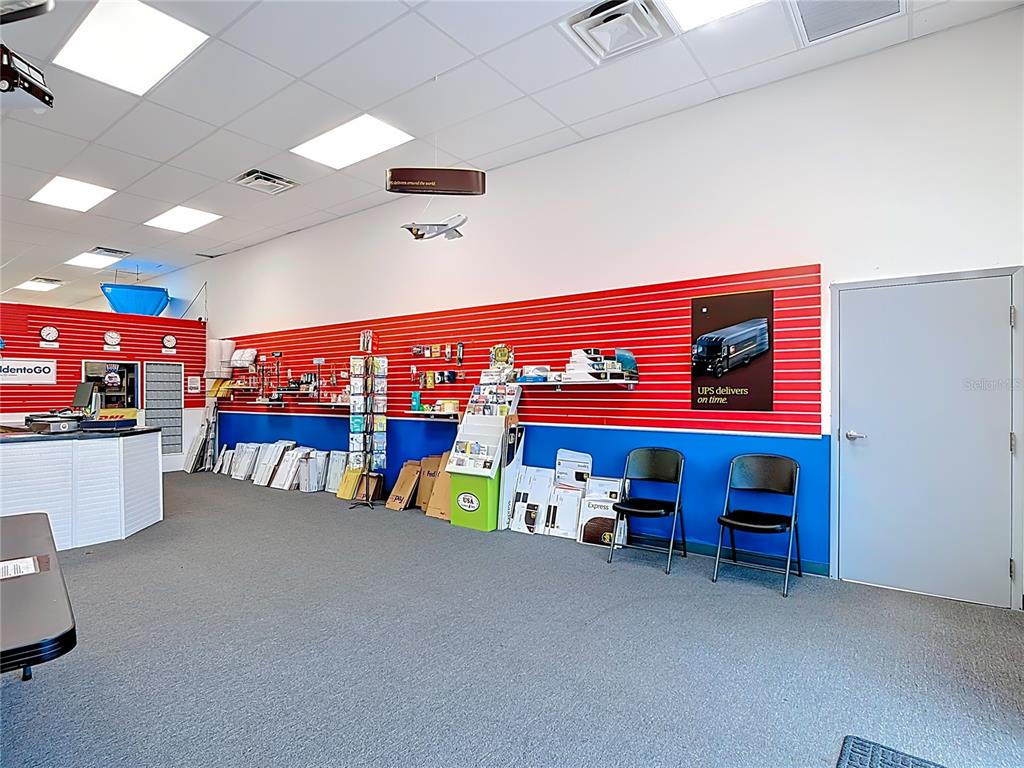 A commercial shipping store interior features red and blue walls, shelving, and two black chairs — 1372 S NARCOOSSEE ROAD, ST CLOUD, FL