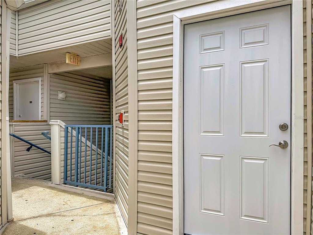 An exterior view shows a white door, beige siding, and a blue metal railing — 2504 WOODGATE BOULEVARD UNIT 203, ORLANDO, FL