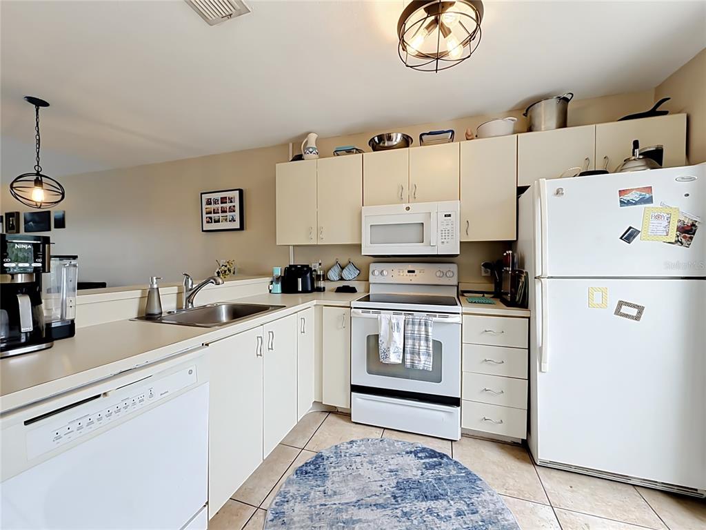 A kitchen features white cabinetry, white appliances, a stainless steel sink, and light-colored tile flooring — 2504 WOODGATE BOULEVARD UNIT 203, ORLANDO, FL