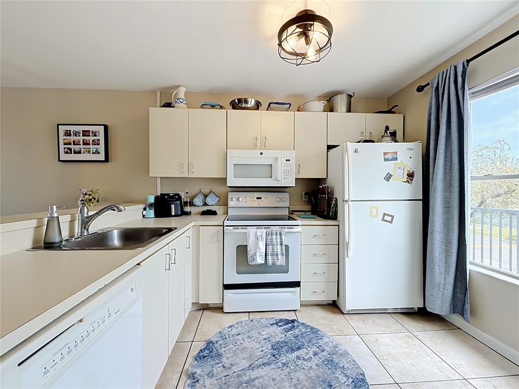 A kitchen features white cabinets, white appliances, a stainless steel sink, and tile flooring — 2504 WOODGATE BOULEVARD UNIT 203, ORLANDO, FL