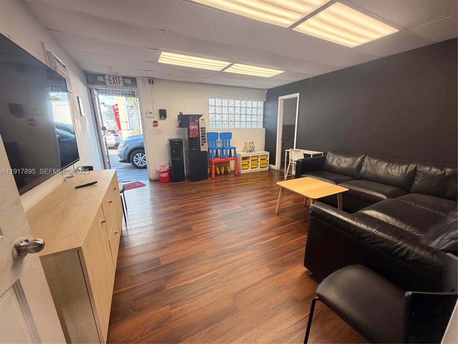 A waiting room features wood flooring, a black leather sectional, a coffee machine, and glass blocks — 7298 NW 54th St, Miami FL 33166, MIAMI, FL