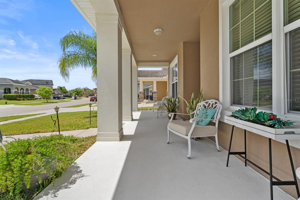 A covered front porch features a white chair, a plant stand, and columns overlooking a street — 2987 BOATING BOULEVARD, KISSIMMEE, FL