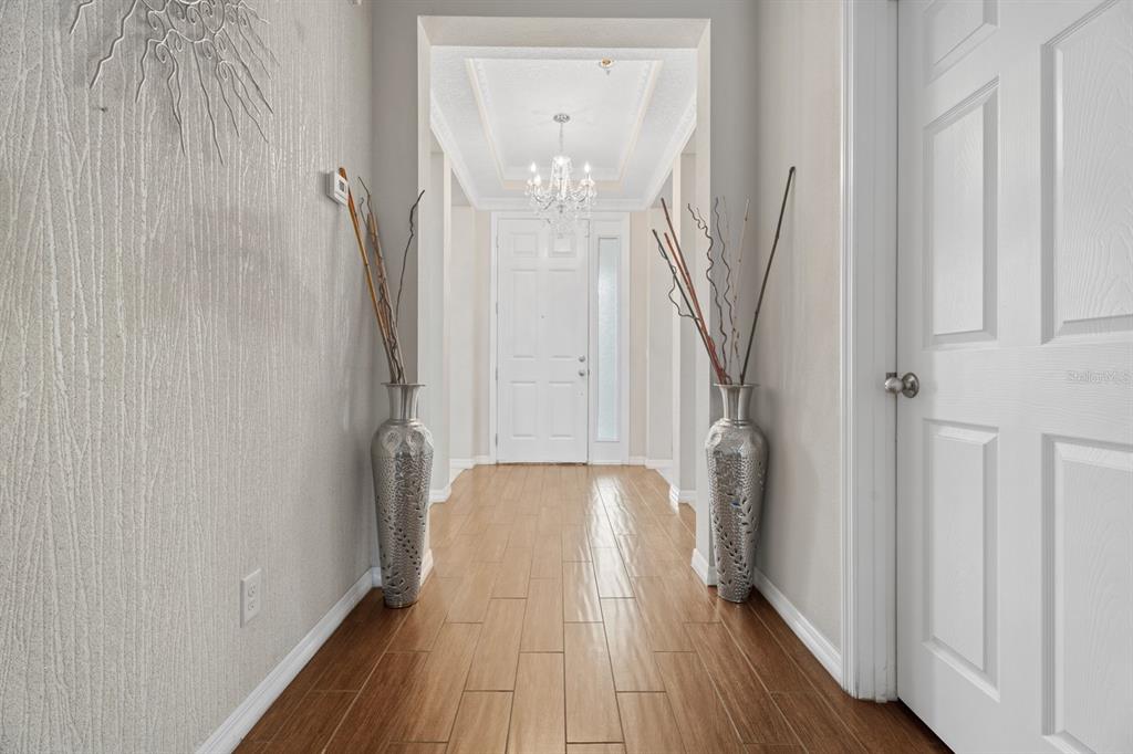 A hallway features wood-look tile flooring, textured gray walls, and two large silver floor vases — 2987 BOATING BOULEVARD, KISSIMMEE, FL
