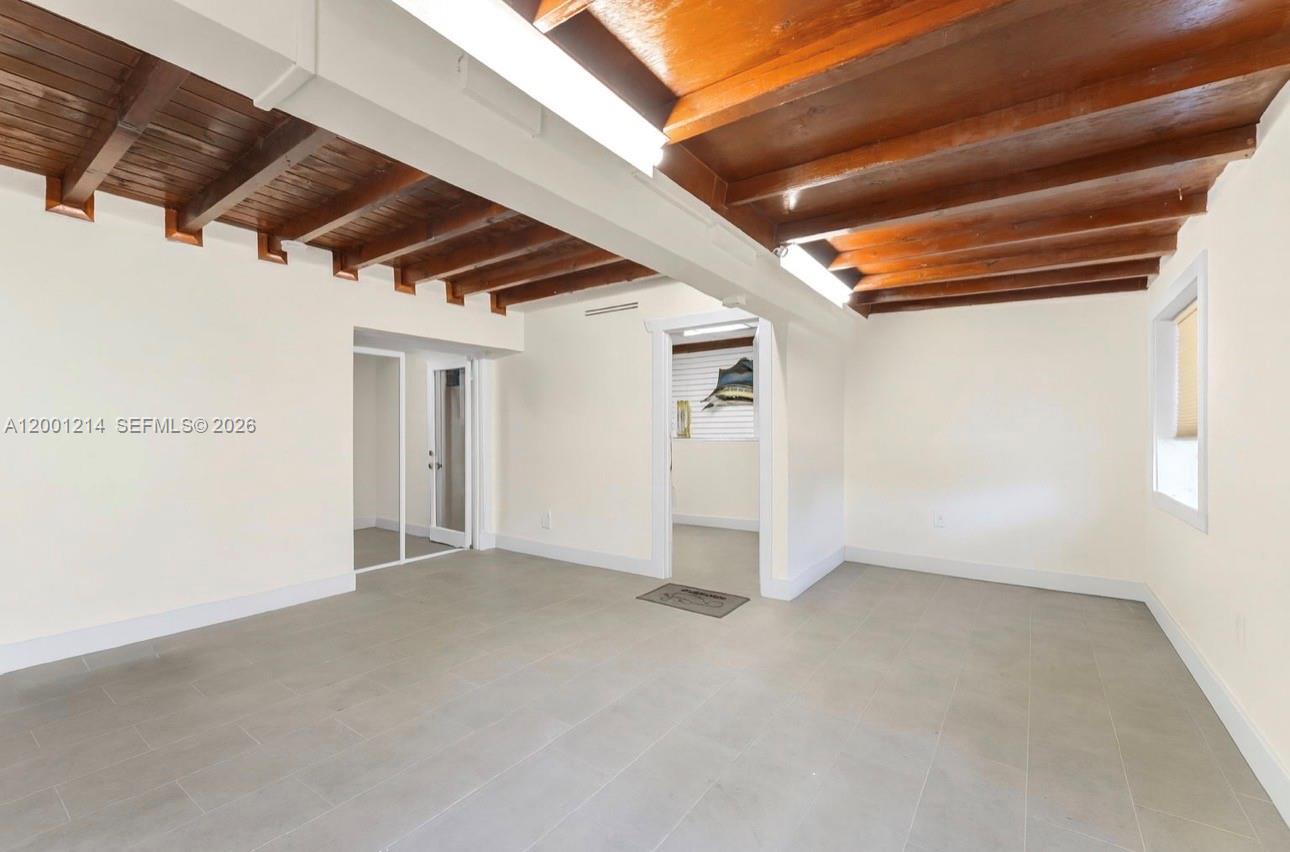 An empty room features exposed wooden ceiling beams, white walls, and light gray tile flooring — 101875 Overseas Hwy, Key Largo FL 33037, KEY LARGO, FL