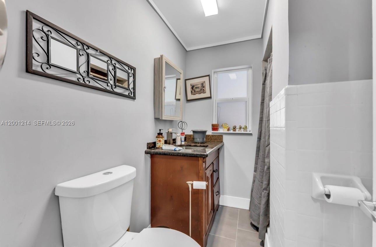 A bathroom features a wooden vanity, a white toilet, and a wall-mounted decorative mirror — 101875 Overseas Hwy, Key Largo FL 33037, KEY LARGO, FL