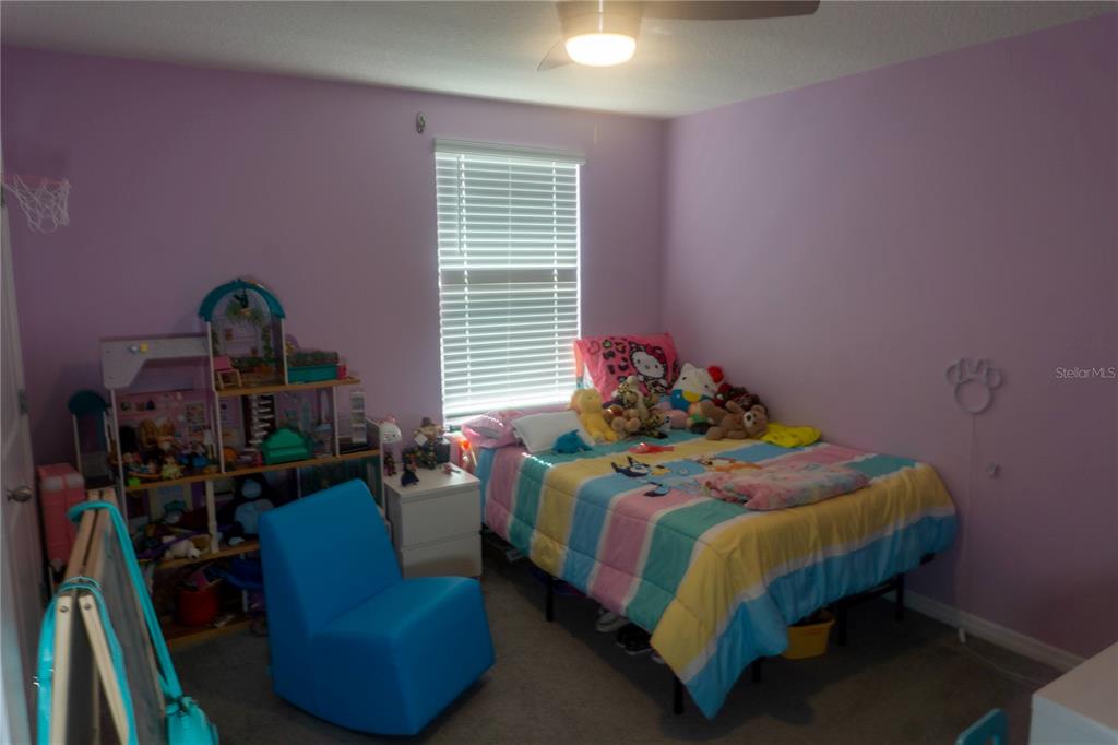 A bedroom with purple walls, a bed with a striped comforter, and a dollhouse — 7819 SAIL CLOVER LANE, ZEPHYRHILLS, FL