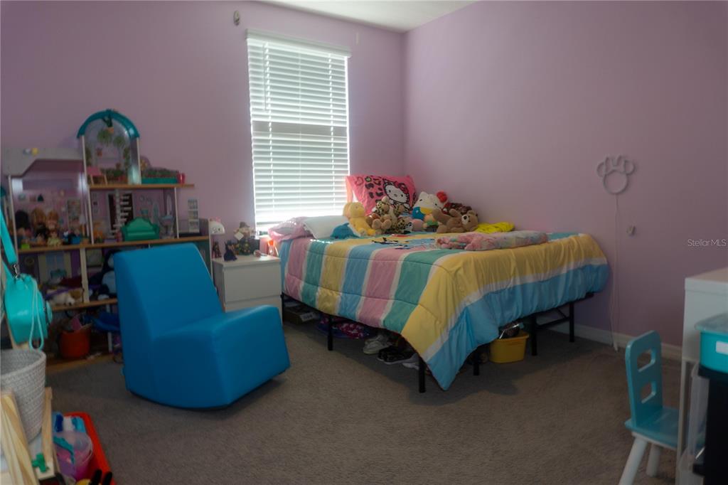 A bedroom with lavender walls, a striped bedspread, a blue chair, and a dollhouse — 7819 SAIL CLOVER LANE, ZEPHYRHILLS, FL