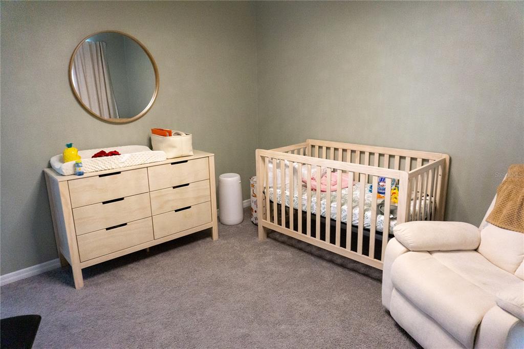 A nursery features a light wood dresser, a matching crib, and a white recliner on carpet — 7819 SAIL CLOVER LANE, ZEPHYRHILLS, FL