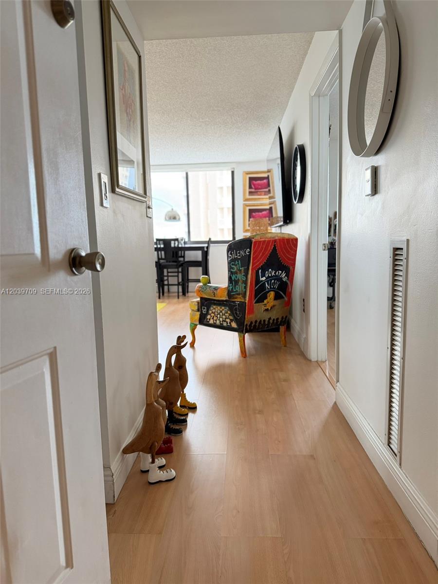 A hallway with light wood flooring leads to a living area featuring a decorative chair — 540 Brickell Key Dr # 828, Miami FL 33131, MIAMI, FL
